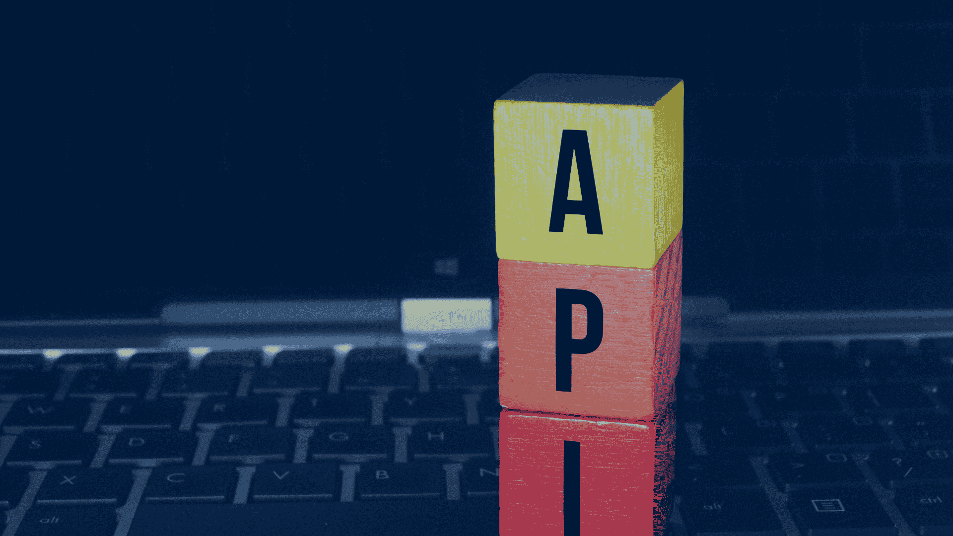 Colorful wooden blocks spelling “API” stacked on a laptop keyboard, symbolizing software connectivity and digital integration