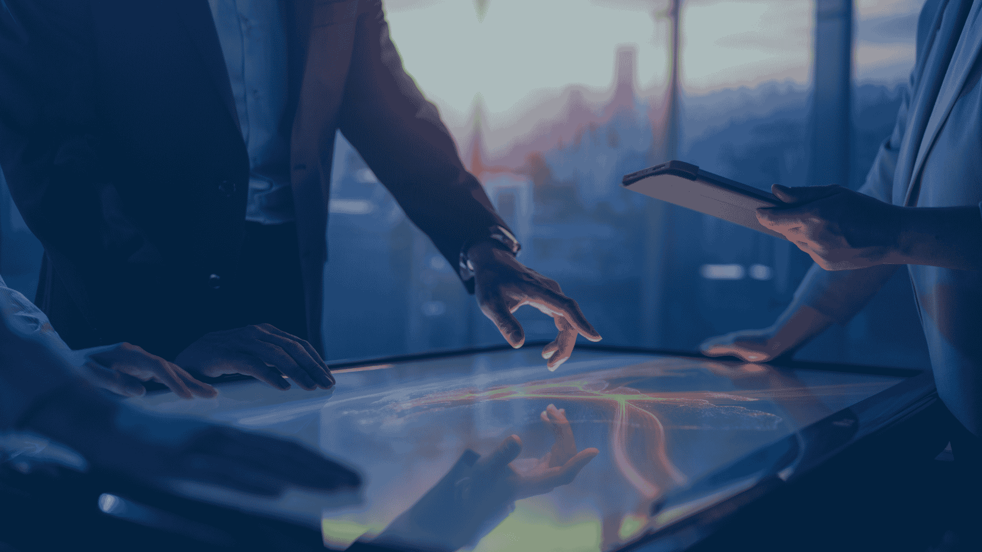 Colleagues gather around a glowing touchscreen table at sunset, one pointing at the screen while another holds a tablet.